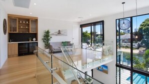A modern interior with a kitchen, living area, and a glass bridge to a balcony with a pool view. - Relax, Chill, Enjoy and Luxury all comes in this Property! (Gold Coast)