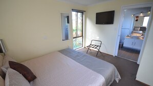 Un dormitorio con cama, una silla, televisión y baño visible a través de una puerta abierta.