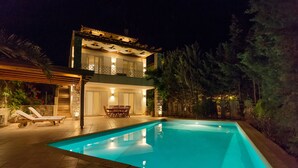 Una casa de dos pisos con piscina, mobiliario exterior y un balcón bien iluminado.
