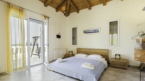 Un dormitorio con una cama grande, techo de madera, puerta corrediza de vidrio, una mesita de noche y un ventilador de pared.
