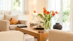 Una sala de estar con una mesa de centro de madera, un jarrón con tulipanes anaranjados, un jarrón oscuro y un sofá con un cojín.