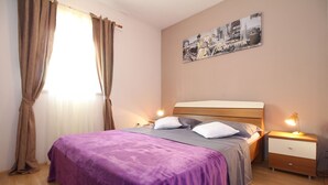 Une chambre à coucher comprenant un lit, deux tables de chevet, une commode, un tableau accroché au mur et une fenêtre avec des rideaux.