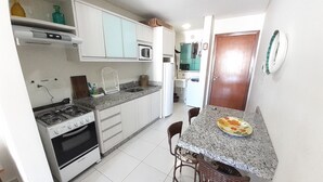 Een compacte keuken met witte kasten, een gasfornuis, een magnetron en een spoelbak. Er is een eethoek met een tafel en stoelen.
