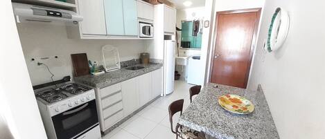 A compact kitchen with white cabinets, a gas stove, a microwave, and a sink. There is a dining area with a table and chairs.