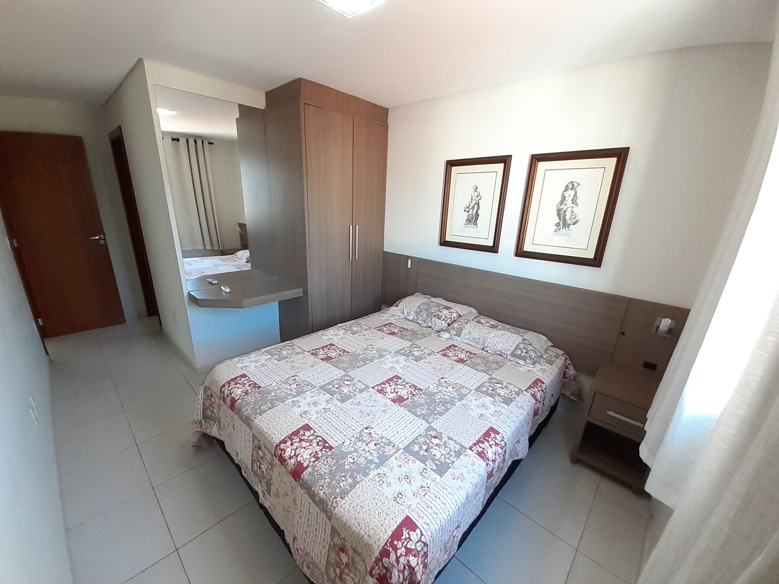 Une chambre à coucher comprenant un lit, une table de chevet, une armoire, un miroir et deux tableaux encadrés accrochés au mur.