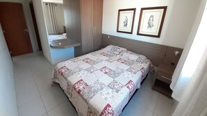 Een slaapkamer met een bed, nachtkastje, kledingkast, spiegel en twee ingelijste foto’s aan de muur.