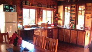 Interior em madeira com cozinha, mesa de jantar e cadeiras.