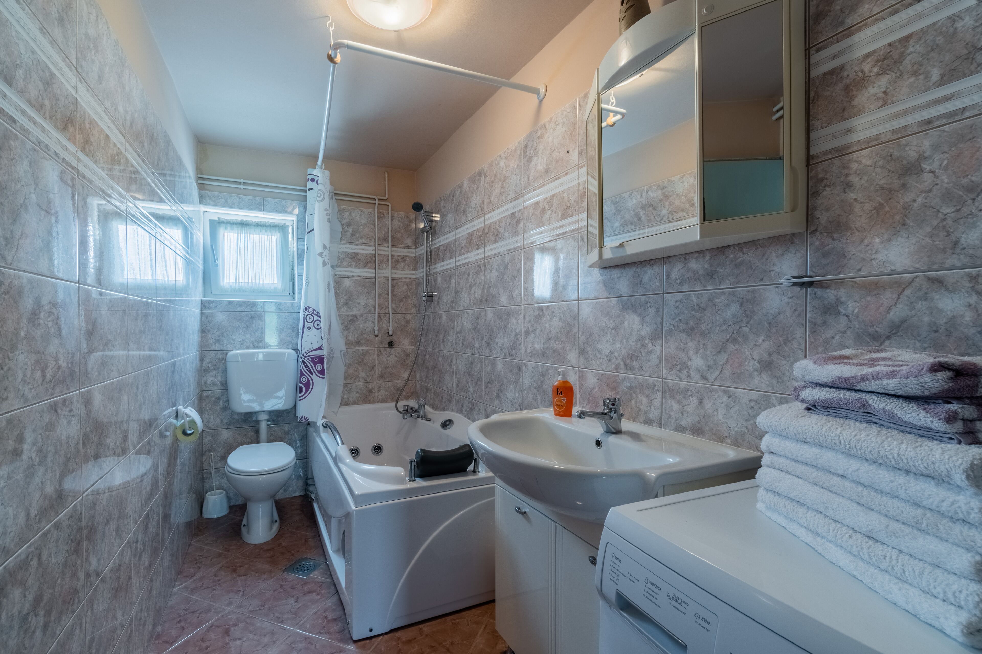 A modern bathroom with a toilet, shower, bathtub, sink, and a stacked towel rack.