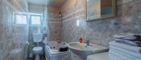 A modern bathroom with a toilet, shower, bathtub, sink, and a stacked towel rack.