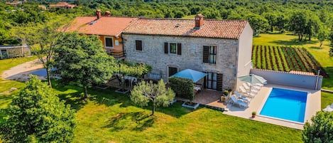 Una casa in pietra con tetto in tegole, una piscina e un giardino con alberi e prato.