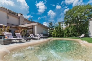 A swimming pool with lounge chairs and umbrellas, surrounded by a building with a flat roof and a clear blue sky. - Apartments Bego Spa & Wellness, Palma (Crikvenica)
