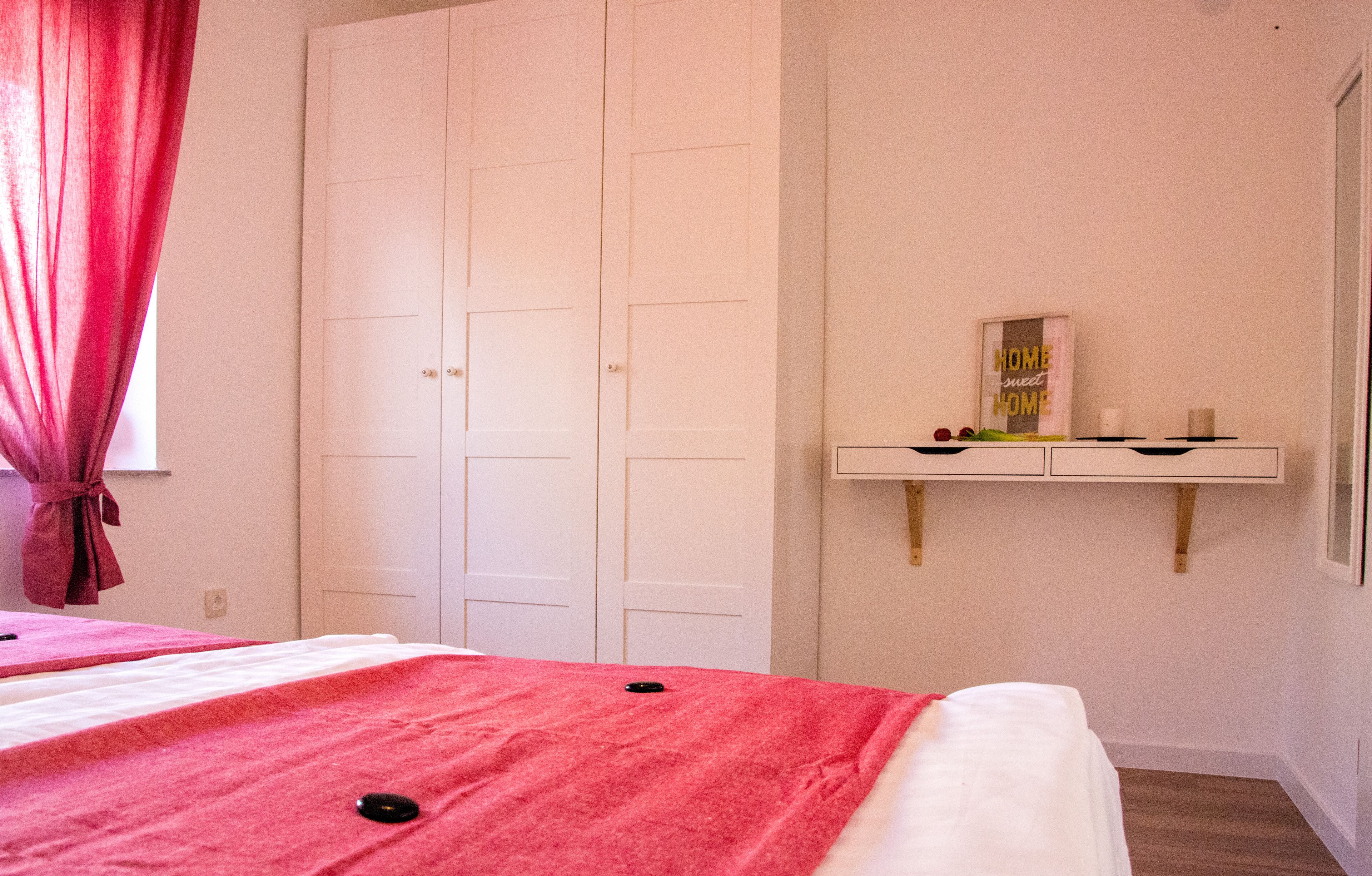 Ein Schlafzimmer mit Bett, Kleiderschrank, Schminktisch mit Spiegel und einer Ablage mit Dekoration.