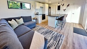 Un espace de vie moderne avec un canapé gris, un petit coin cuisine et un bar avec des tabourets.