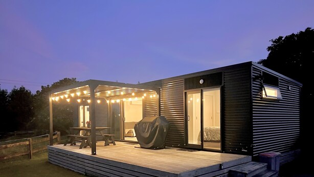 Une maison moderne de plain-pied, dotée d’un patio couvert, d’un barbecue et d’une grande porte-fenêtre coulissante.
