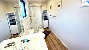 Une salle de bain moderne avec une douche à parois de verre, un lavabo blanc doté de robinetterie chromée et un plancher en bois.