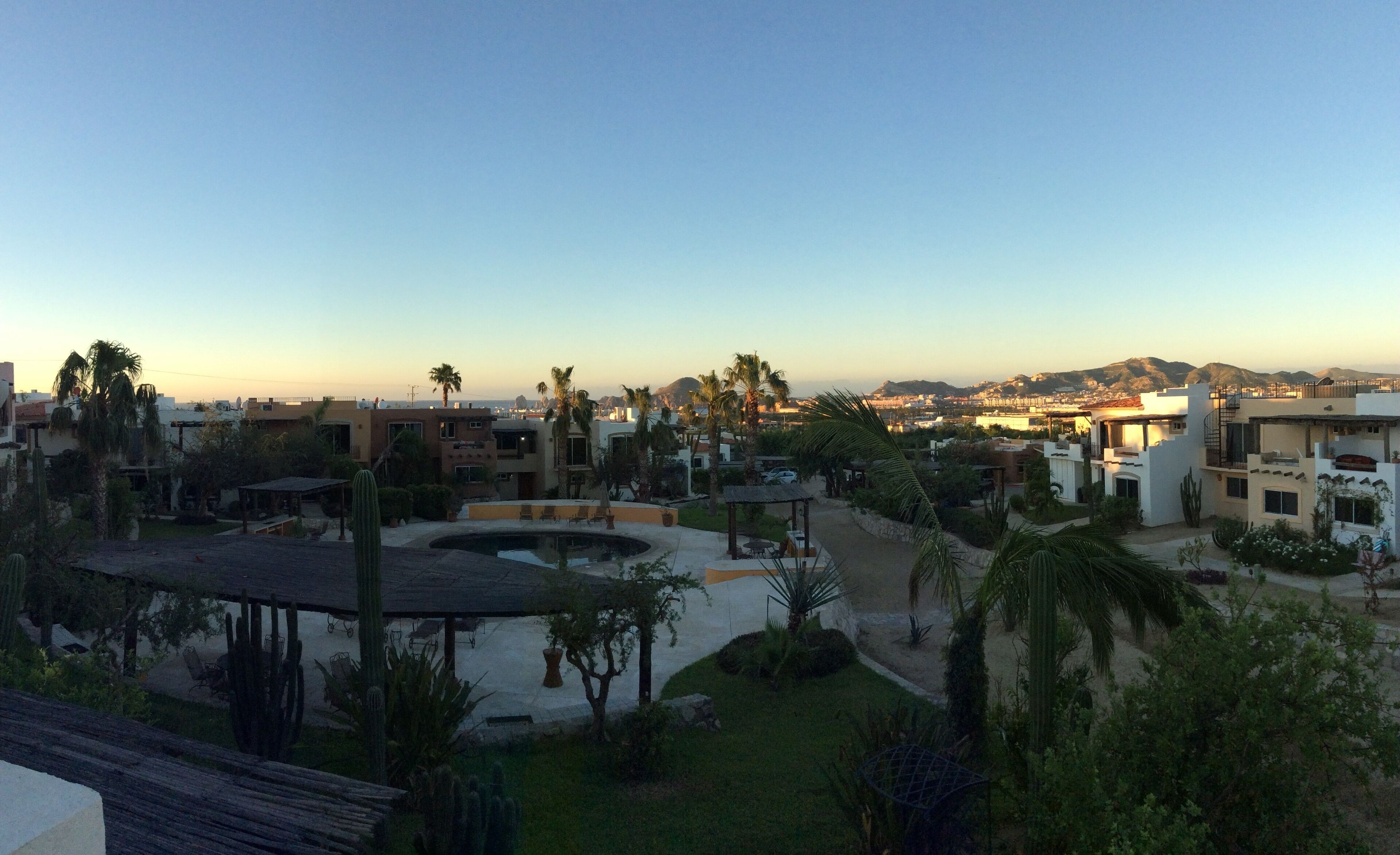 A resort with a pool, palm trees, and a view of the city and mountains.