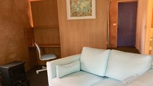 A room with a light blue sofa, a small wooden cabinet, a chair, and a map on the wall. - Frogsong Strawbale Cottage BLUE | Mansfield (Mountain Bay)