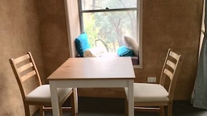 A small room with a window, a wooden table, two chairs, and a blue pillow on the window sill. - Frogsong Strawbale Cottage BLUE | Mansfield (Mountain Bay)