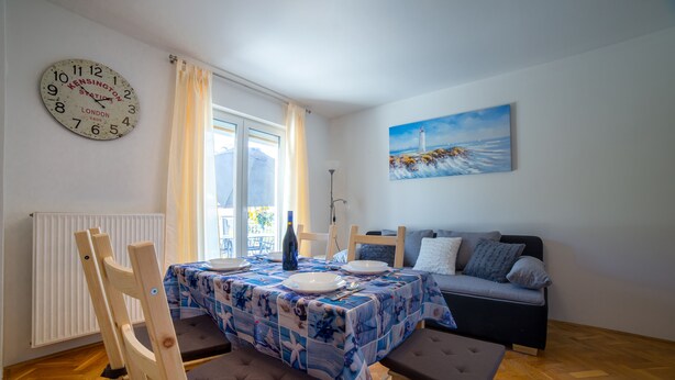 Un coin repas avec une table dressée pour deux personnes, un canapé et un tableau accroché au mur.