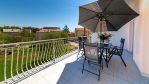 Un balcon avec une table et des chaises, un grand parasol et une vue sur le quartier.
