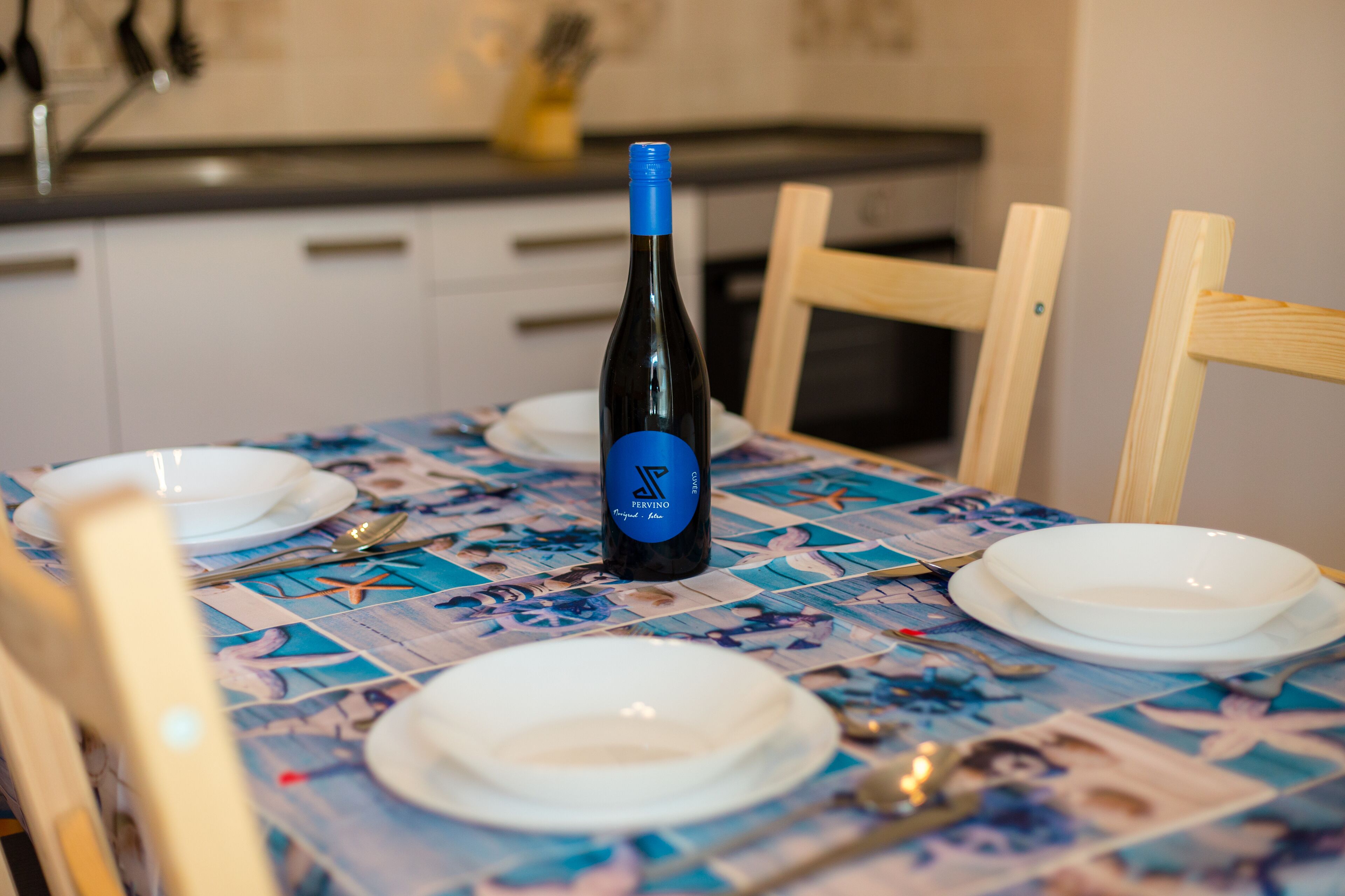 A dining table with a bottle of wine, plates, and cutlery.