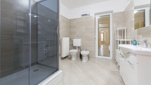 Une salle de bain moderne avec une douche à parois de verre, deux toilettes et un meuble-lavabo blanc avec un miroir.