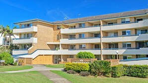 A multi-story apartment building with a brick facade, multiple balconies, and a well-maintained lawn.