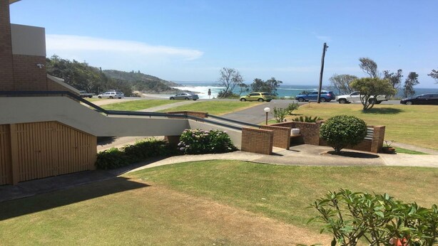 A residential area with a driveway leading to a house, a small garden, and a view of the ocean.