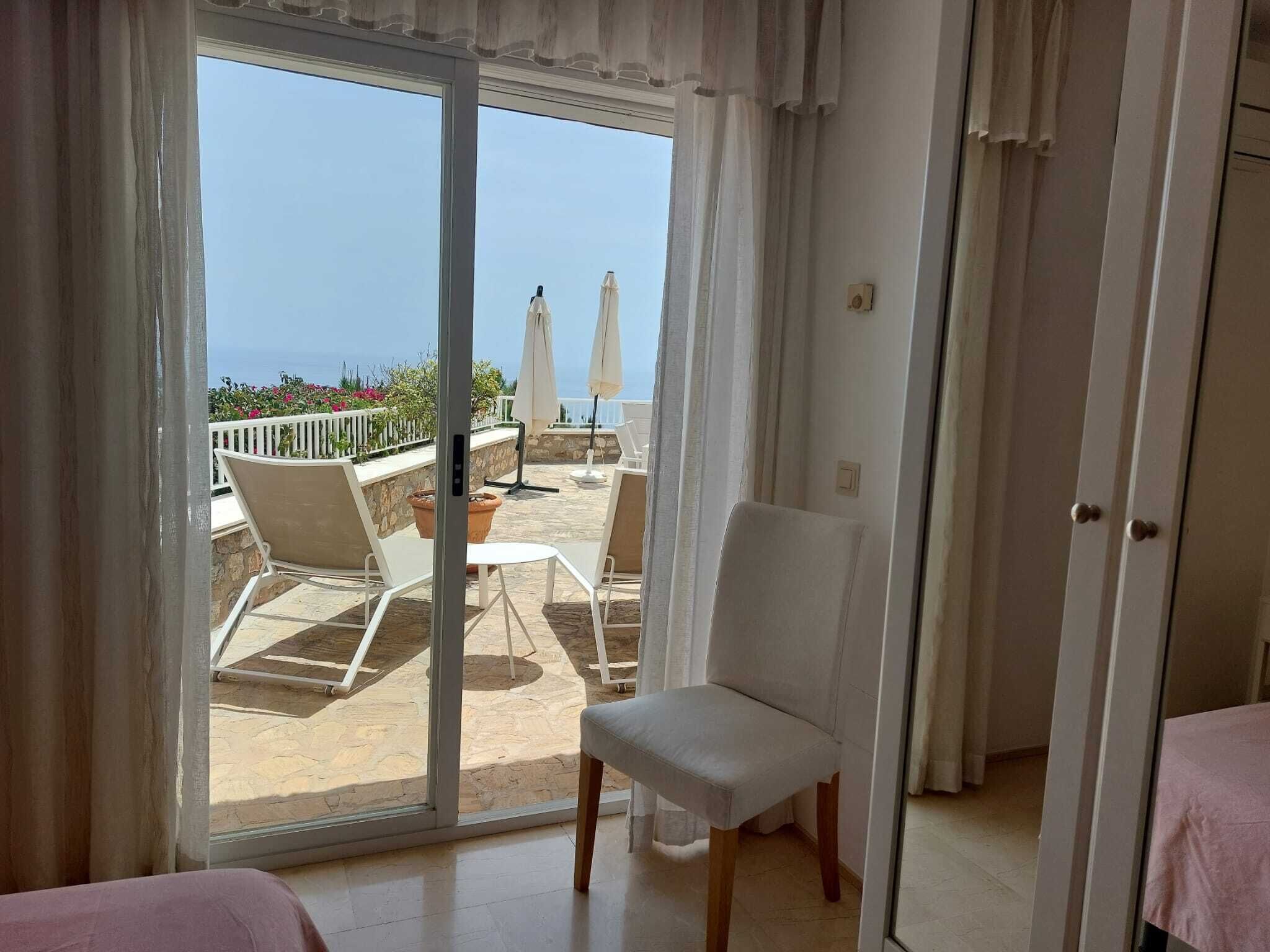 Una stanza con una porta scorrevole in vetro che dà su un'area salotto esterna con vista sul mare.