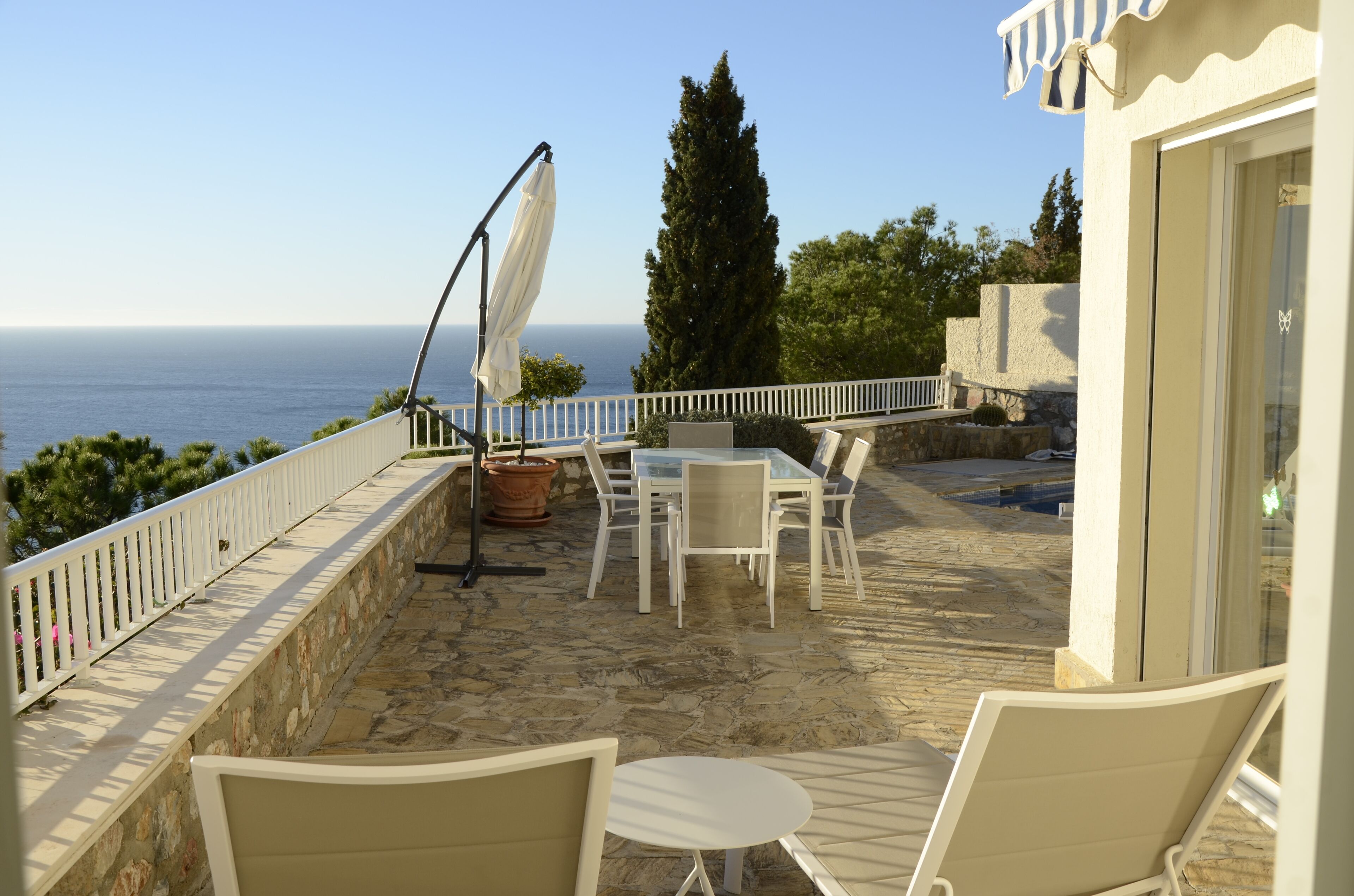 A terrace with a stone floor, white furniture, and a view of the sea.