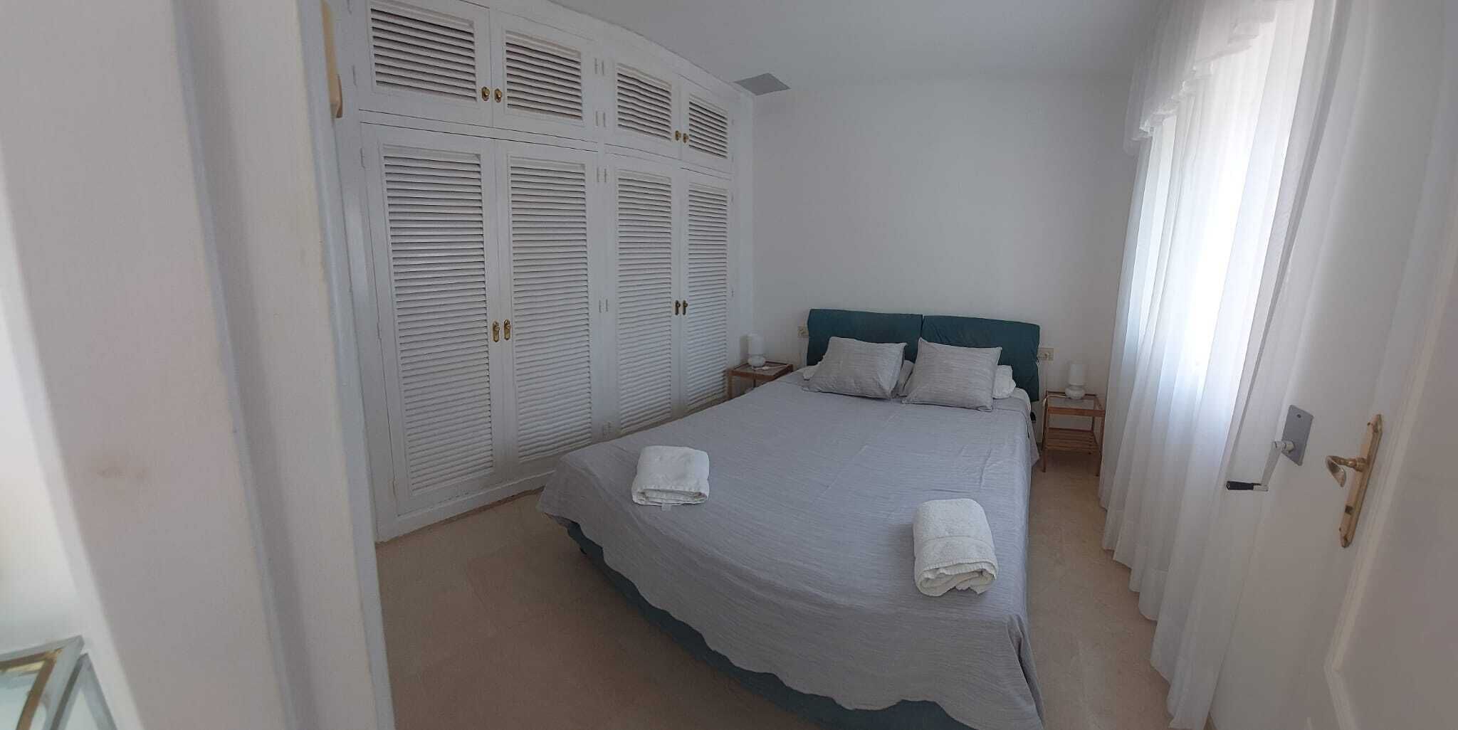 A bedroom with a bed, two nightstands, a headboard, and a set of white louvered closets.