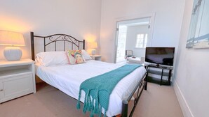 A bedroom with a bed, two bedside tables, a TV, and a large mirror.