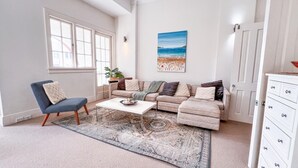 A living room with a large window, a beige sofa set, a coffee table, and a white dresser.