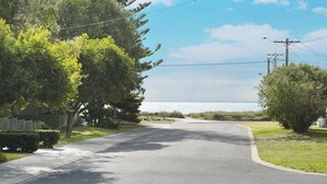 A residential street with a curved road leading to a body of water. - SHELLEBRATIONS - Endless Summer (West Busselton)