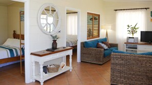 A furnished room with a bed, a console table, a wicker sofa, a television, and a window with curtains.