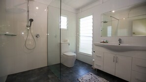 A modern bathroom with a glass shower enclosure, a white toilet, a vanity with a mirror, and a dark floor.