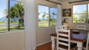 A dining area with a table and chairs, large windows with a view of the outdoors, and a painting on the wall.