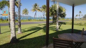 A covered outdoor area with a table and bench, surrounded by palm trees and a view of the ocean.