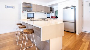 Une cuisine moderne dotée d’un îlot central, de tabourets de bar, d’un réfrigérateur et d’un panneau indiquant l’emplacement d’une plage.
