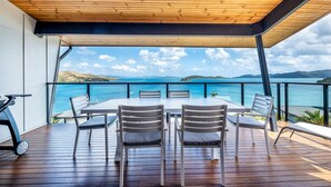 Une terrasse en bois avec une table et des chaises, d’où l’on peut admirer un plan d’eau et des collines lointaines.
