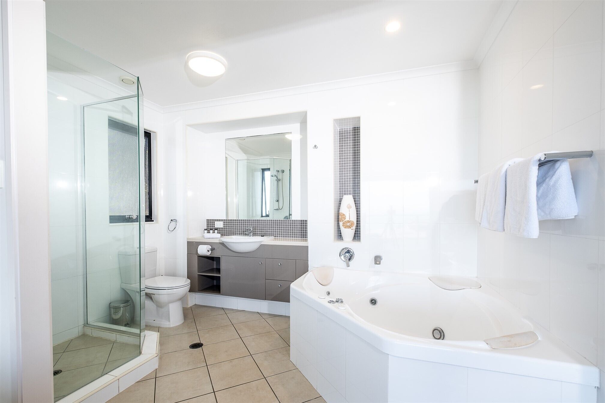A modern bathroom with a glass shower enclosure, a white toilet, a sink with a mirror above it, and a large bathtub.