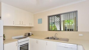A compact kitchen with white cabinets, a stove, a dishwasher, and a window with a metal grill.