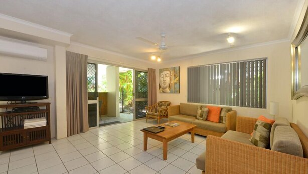 A living room with a flat-screen TV, a sofa, a coffee table, and a ceiling fan.