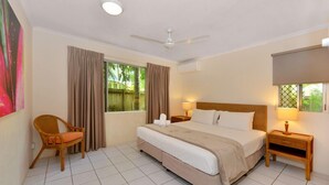 A hotel room with a bed, a chair, a nightstand, a ceiling fan, and a window with curtains.
