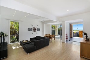 Relax in a welcoming space with a sleek sofa and dining table, surrounded by lush views and an open-plan layout connecting to a spacious patio.