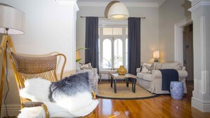 A living room with a large window, a sofa, a chair, and a lamp. - Camellia Cottage - Beautiful 3 bedroom cottage with gorgeous gardens - stroll to local cafes! (Cessnock)