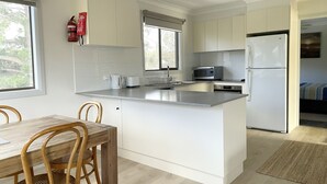 A modern kitchen with white cabinetry, a central island, a microwave, and a refrigerator. - Self contained Top Unit - Surfs Up - Hear the sea at night. (Broulee)