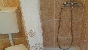 A bathroom with a toilet, a shower with a handheld showerhead, and a patterned shower curtain. - Cosy apartments surrounded with green space (Petrovac)