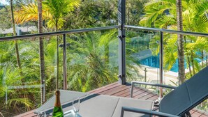 A balcony with a glass table, two chairs, a bottle of champagne, and a glass. The balcony overlooks a pool and lush greenery. - Pinnacle 3, Seaview Apartment on Hamilton Island (Hamilton Island)
