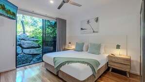 A bedroom with a bed, nightstands, a ceiling fan, and a view of a tropical garden through glass doors. - Pinnacle 3, Seaview Apartment on Hamilton Island (Hamilton Island)